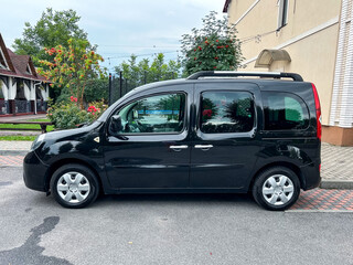 A black compact van is parked outside, nestled within a charming residential area that is...