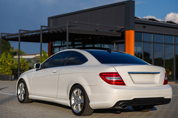 A sleek white luxury coupe is parked outside a modern architectural building, highlighting a blend...