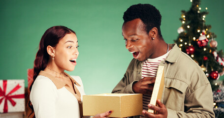Christmas, gift and shocked with interracial couple in studio for holiday season, celebration and...