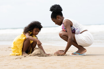 Mother and daughter sculpting sand on tropical beach together. African American tourist family...