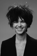 Smiling woman with messy hair wearing a black blazer in black and white studio portrait