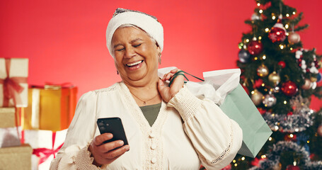 Senior, happy woman and phone with shopping bag for christmas deal on a red studio background....