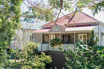 A classic Queenslander-style house with a red roof, elevated veranda, and surrounded by trees, Brisbane, Queensland, Australia