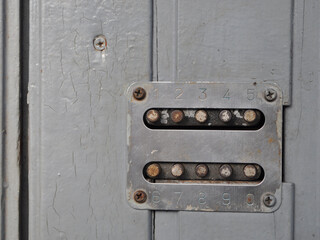 Old metallic code lock panel with worn-out numbered buttons (1–9,0) mounted on a gray painted...