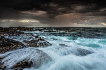 Lorient Morbihan Heavy storm clouds over crashing waves and rugged rocky coastline.