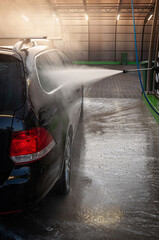 A shiny black car is being washed with high-pressure water jets at a car wash facility.