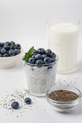 Glass with chia pudding, fresh blueberries, kefir, milk, chia seeds and a bowl with berries. Healthy eating concept, superfood.