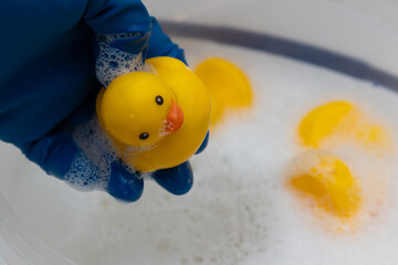 A person wearing a blue glove holds a yellow rubber duck with soap bubbles while others float in a...