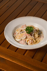 Creamy Ham and Mushroom Pasta. Classic Italian spaghetti with a rich, white sauce, diced ham, and sliced mushrooms, garnished with parsley. Comfort food on a wooden table.