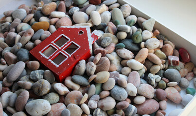 Cardboard Box Filled with Colorful Pebbles Around the Red Toy House 
