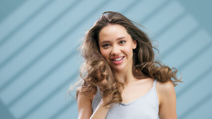 Fototapeta premium Young woman with healthy skin and flowing hair, smiling joyfully against a soft blue background, showcasing natural beauty and confidence in a vibrant skincare concept