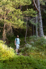 A man walking through the forest surrounded by trees and nature. Concept of hiking, outdoor adventure, exploration, solitude, and connection with the wilderness.