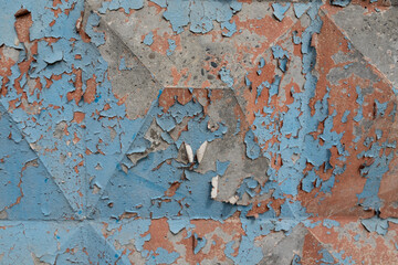 Close-up of a weathered painted metal surface with peeling blue and red paint on geometric embossed...