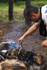A man is lighting a campfire in the forest, creating a warm and cozy atmosphere in the wilderness. Concept of camping, survival, outdoor adventure, and nature connection.