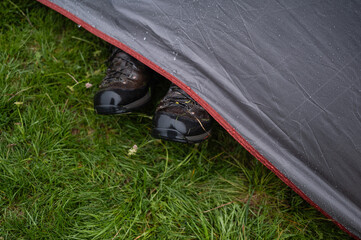 Hiker resting with feet out of tent on grass during rain