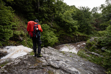Hiker contemplating waterfall in lush green forest