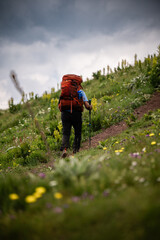 Hiker walking up green mountain trail on cloudy day