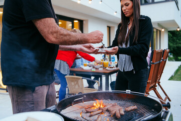 A group of friends and family barbecue together in the evening on the terrace in front of a large...
