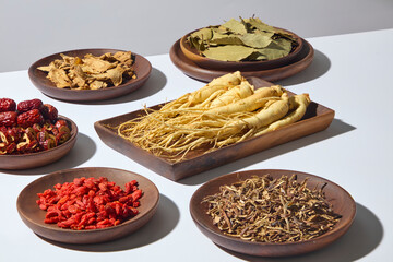 An arrangement of fresh ginseng roots with goji berries and herbal ingredients on round wooden plates. The warm light emphasizes natural details and textures.