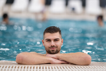 Man resting on the edge of a large indoor pool with a calm expression and relaxed posture.