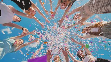 High school graduates joyfully tossing confetti in the air against a backdrop of clear blue sky