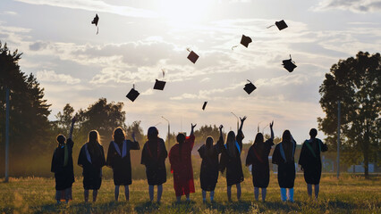 Group of graduates throwing mortarboards in the air at sunset, celebrating their academic...