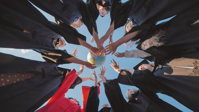 Group of graduates in academic gowns forming a circle, holding a globe, symbolizing global education and future opportunities