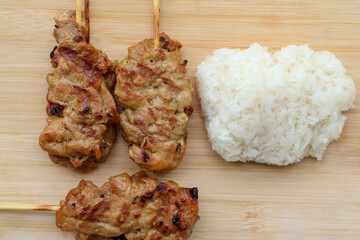 High angle view of Grilled pork skewers and sticky rice on a wooden tray. Thai street food