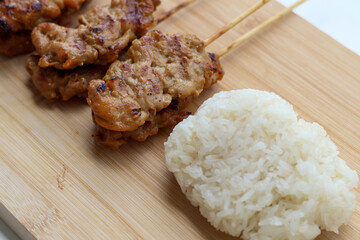 Closeup view of Grilled pork skewers and sticky rice on a wooden tray
