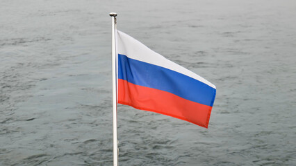 Russian flag waving vigorously, billowing against muted grey waterscape, symbolizing national...