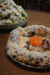 Gourmet pizza with runny egg yolk, parmesan cheese, and fresh salad served in restaurant.