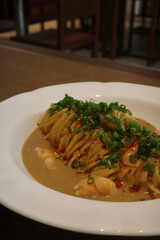 Creamy pasta with shrimp, scallions, and spicy sauce served in a white bowl at restaurant.