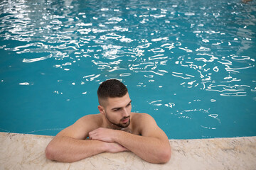 Man resting on the edge of a large indoor pool with a calm expression and relaxed posture.