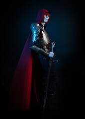 Naklejka premium Fantasy warrior woman with red hair in historical medieval armour costume and red fairytale cloak, cinematic studio portrait of strong heroine knight, dramatic standing profile silhouette figure.