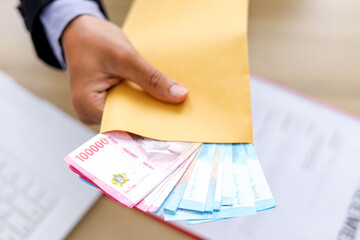Hand Holds a Yellow Envelope Revealing Colorful Indonesian Rupiah Banknotes Inside