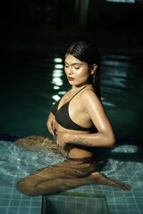 Fototapeta premium Woman Sitting in Swimming Pool with Upper Body Above Water in Bikini Portrait 
