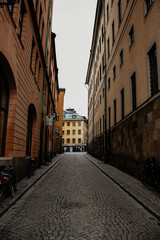 A narrow cobblestone street in Stockholm's old town, Gamla Stan, lined with historic buildings under an overcast sky.
