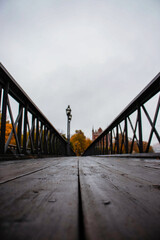 A low-angle view along a wooden plank bridge with black iron railings, stretching through an...