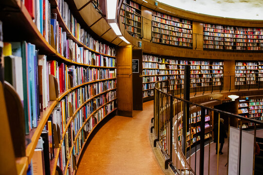 A wide-angle shot of a beautiful, circular library interior with countless books lining curved wooden shelves and a person standing below.