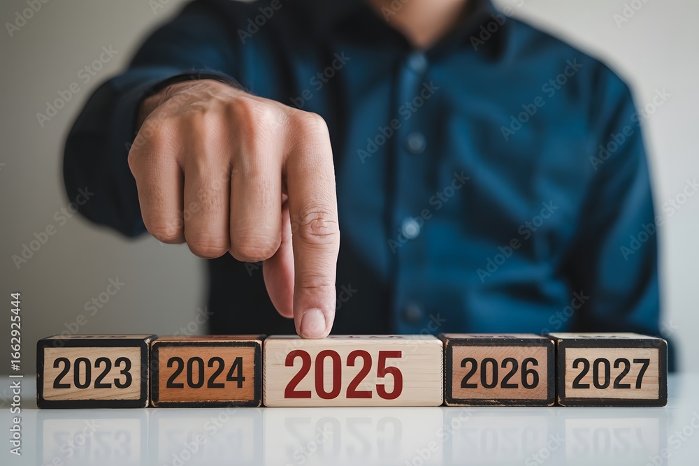 Poster a person points at a wooden block with the year 2025 among a row of blocks showing future years