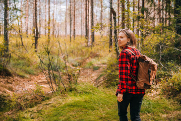A girl in a red shirt and with a backpack is walking in the forest. Hiking in sunny autumn forest.