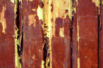 rusted, weathered yellow-painted metal panels. The panels show extensive peeling and flaking,...