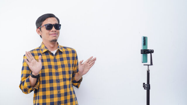 Asian young man recording video content, dancing on smartphone camera at studio. Positive millennial filming for social media, using mobile device. - Powered by Adobe