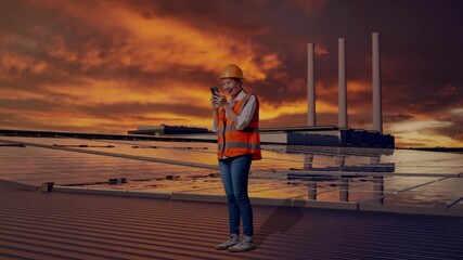 Full Body Side View Of Asian Female Engineer With Safety Helmet Using Smartphone While Standing, Inspecting Solar Panels on Rooftop at Sunset - Powered by Adobe