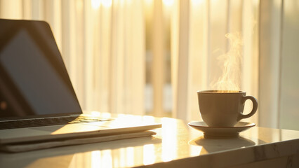 Laptop and steaming coffee cup on a marble table near a window with soft sunlight and white curtains in a warm setting