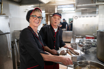 Two chefs in black uniforms working together while serving freshly fried fish in a commercial kitchen. Concept of seafood preparation, teamwork, culinary skills, and hospitality industry.