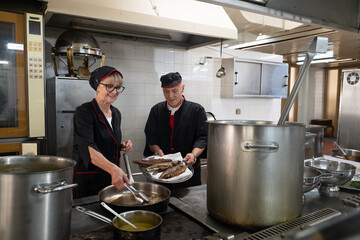 Two chefs in black uniforms working together while serving freshly fried fish in a commercial...