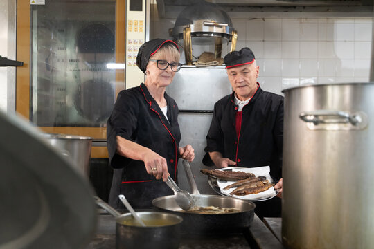 Two chefs in black uniforms working together while serving freshly fried fish in a commercial kitchen. Concept of seafood preparation, teamwork, culinary skills, and hospitality industry. - Powered by Adobe
