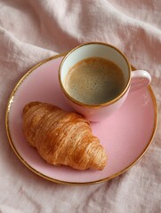 Pink coffee cup and croissant on a linen tablecloth