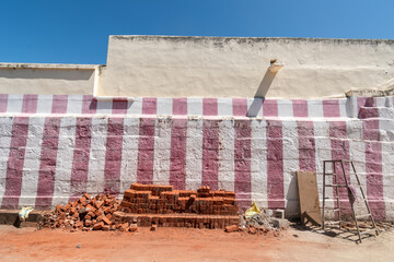 Brightly colored striped wall features stacked bricks in front, showcasing a construction area on a sunny day.